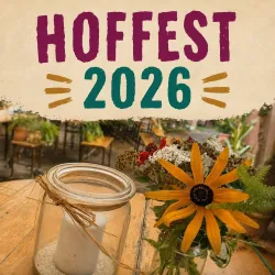 Ein fröhliches Festmotiv mit der Aufschrift "Hoffest 2026". Ein Glas mit einer Kerze und ein bunter Blumenstrauß schmücken den Tisch.