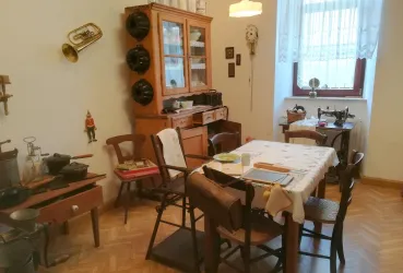 Ein gemütliches, traditionelles Esszimmer mit einem Holztisch und Stühlen. Über der Anrichte sind Kochutensilien und Dekorationen zu sehen.