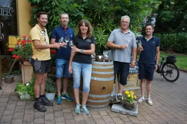 Eine Gruppe von fünf Personen steht lächelnd vor einer Fässer und Blumen. Im Hintergrund sind Pflanzen und Rad zu sehen.