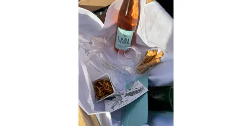 Eine stilvolle Auswahl an Getränken und Snacks, darunter eine Flasche Roséwein und Gläser. Dazu liegen Brezeln und eine hübsch gestaltete Verpackung.