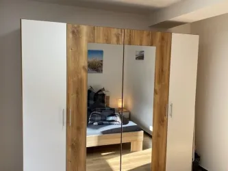Ein moderner Kleiderschrank mit Spiegeln steht in einem gemütlichen Schlafzimmer. Im Hintergrund sieht man ein Bett und sanfte Beleuchtung.
