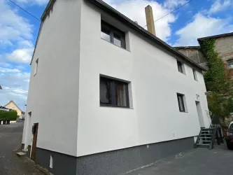 Ein schlichtes, weißes Haus mit modernen Fenstern. Die Fassade ist sauber und gut erhalten, umgeben von einer ruhigen Straße.