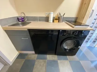 Eine moderne Küchenzeile mit einer Spüle und einem Kochfeld. Rechts befindet sich eine Waschmaschine in schwarzem Design.