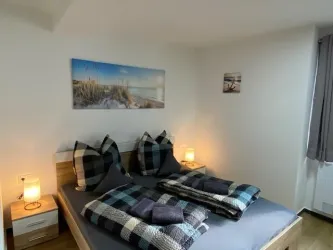 Ein gemütliches Schlafzimmer mit einem Doppelbett, künstlerischen Bildern an der Wand und sanfter Beleuchtung. Die Bettwäsche ist in blauen und grauen Tönen gehalten.