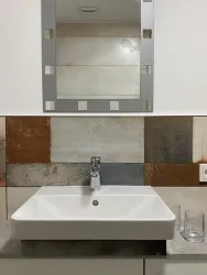 Ein modernes Waschbecken mit einem schlichten Design und einem großen Spiegel darüber. Die Wand ist mit interessanten, rustikalen Fliesen in verschiedenen Farben dekoriert.