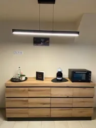 Eine modern gestaltete Küchenzeile aus Holz mit einem eleganten Beleuchtungselement. Auf der Arbeitsfläche befinden sich eine Mikrowelle, ein Mixer und eine Flasche Wasser.