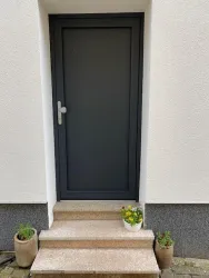 Eine moderne graue Tür mit einem schlichten Design. Auf den Stufen stehen einige Pflanzentöpfe mit floralen Akzenten.