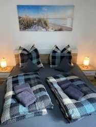 Ein gemütliches Schlafzimmer mit einem Doppelbett und bunten Decken. An der Wand hängt ein Bild von einem Strand bei Sonnenlicht.
