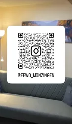 Ein gemütliches Wohnzimmer mit einer grauen Couch und sanfter Beleuchtung. Im Vordergrund befindet sich ein QR-Code, der zu einem Instagram-Profil führt.