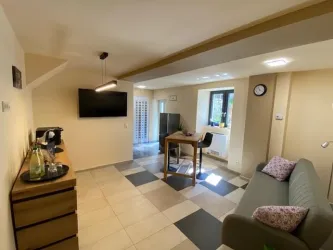 Ein modern eingerichteter Wohnraum mit einem Sofa, Tisch und einem Fernseher an der Wand. Das Raumdesign ist hell und freundlich, mit großen Fenstern für natürliche Beleuchtung.