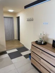 Ein heller Flur mit einem Holzschrank und einem Boden aus Fliesen. An der Wand hängen Garderobenhaken und eine Tür führt zu einem weiteren Raum.