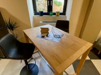 Ein moderner Essbereich mit einem Holztisch und zwei Stühlen. Auf dem Tisch befindet sich eine Dekoration und Blick auf die Pflanzen am Fenster.