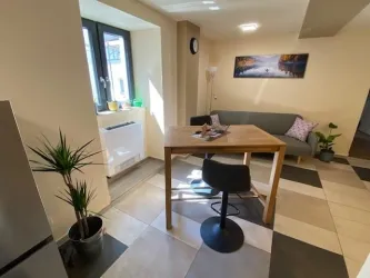 Eine moderne Küche mit einem Tisch und einem Stuhl. Im Hintergrund stehen Pflanzen und ein Sofa, während ein Bild an der Wand hängt.