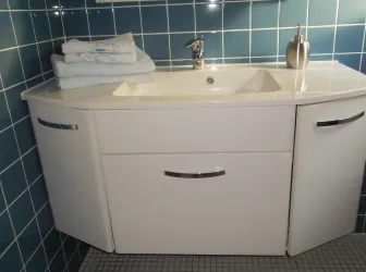 Ein modernes Waschbecken mit weißem Möbel und zwei Schubladen. Im Hintergrund sind blaue Fliesen zu sehen und es liegen gefaltete Handtücher darauf.