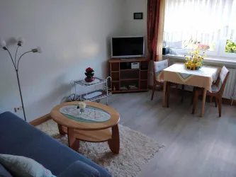 Ein gemütliches Wohnzimmer mit einem blauen Sofa und einem Tisch. In der Ecke steht ein Fernseher und ein Tisch mit Blumenarrangement.