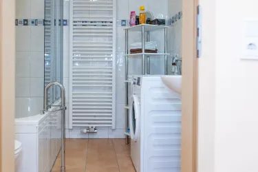 Ein modernes Badezimmer mit einer Badewanne und einer Waschmaschine. Im Hintergrund sind Regale mit Pflegeprodukten und Handtüchern.