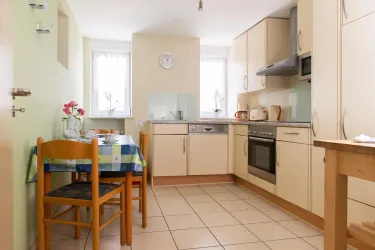 Eine moderne Küche mit hellen Möbeln und einem Tisch mit Stühlen. Die Wände sind in sanften Farben gestrichen und es gibt viel natürliches Licht.