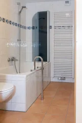 Ein modernes Badezimmer mit einer Badewanne und Dusche. Es gibt helle Fliesen und einen Handtuchheizkörper.