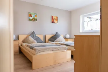 Ein helles Schlafzimmer mit zwei Einzelbetten und modernen Kunstwerken an der Wand. Die Möbel sind aus hellem Holz und der Raum wirkt freundlich und einladend.