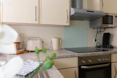 Eine moderne Küche mit hellen Schränken und einer großen Arbeitsfläche. Im Hintergrund sind verschiedene Küchengeräte wie ein Wasserkocher und eine Kaffeemaschine zu sehen.