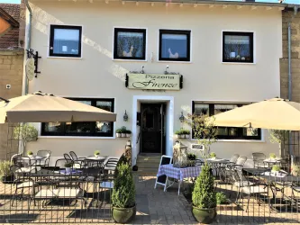 Ein einladendes Restaurant mit einem Außenbereich, der mit Tischen und Sonnenschirmen ausgestattet ist. Die Fassade des Gebäudes ist hell und freundlich gestaltet.