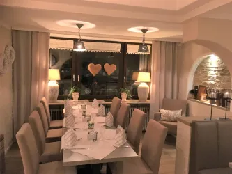 Ein elegantes Restaurant mit einem langen Tisch, der für Gäste gedeckt ist. Sanfte Beleuchtung und herzliche Dekoration schaffen eine gemütliche Atmosphäre.