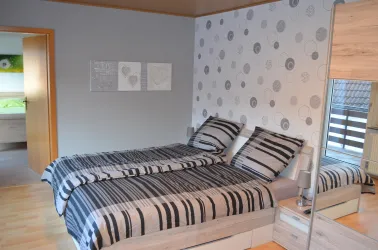 Ein modernes Schlafzimmer mit einem double Bett und gestreiften Bettwäsche. An der Wand sind dekorative Bilder und es gibt einen großen Spiegel.