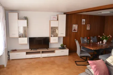 Ein modernes Wohnzimmer mit einem Fernseher und einer hellen Couch. Der Essbereich ist mit einem Holztisch und eleganten Stühlen ausgestattet.