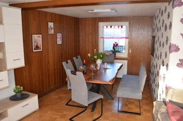 Ein gemütlicher Essbereich mit einem Holztisch und grauen Stühlen. Die Wände sind mit Holzvertäfelung und Blumenmuster dekoriert.
