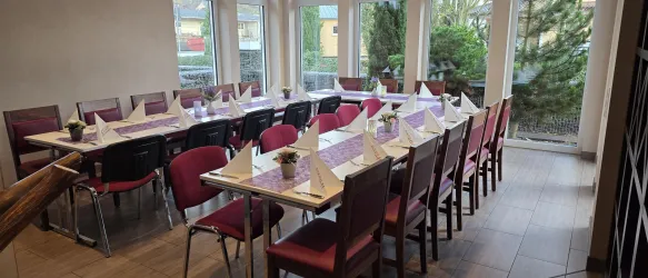 Ein eleganter Speiseraum mit einem langen Tisch, der für ein Treffen gedeckt ist. Durch die Fenster schaut man in einen Garten.