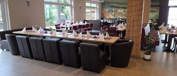 Ein modernes Restaurant mit eleganten Tischen und Stühlen. Die Tische sind für Gäste gedeckt und haben Servietten und Blumenarrangements.