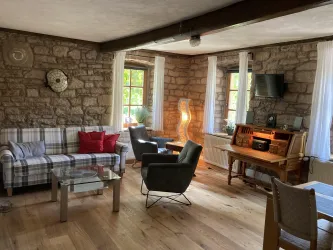 Ein gemütliches Wohnzimmer mit Steinwänden und Parkettboden. Es gibt ein Sofa, Sessel und einen Sekretär aus massivem Kirschholz.