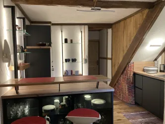 Eine moderne Küche mit Holzdetails und einem offenen Raumkonzept. Der Bartresen ist mit roten Stühlen ausgestattet und es gibt Regale mit Gläsern und Geschirr.