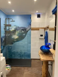Ein modernes Badezimmer mit einer Duschabtrennung, die eine Schildkröte zeigt. Die Einrichtung ist mit Holzdetails und einer blauen Waschschüssel gestaltet.