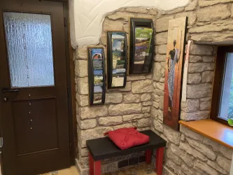 Ein einladender Eingangsbereich mit einer Steinwand und einer Holzbank. An der Wand hängen Informationsblätter und ein dekoratives Kunstwerk.