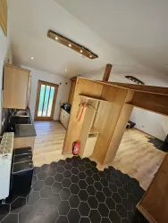 Eine moderne Küche mit Holzdetails und einem hellen Boden. Die Wände sind neutral, und große Fenster sorgen für viel Licht.