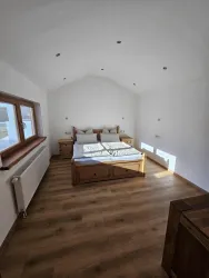Ein helles Schlafzimmer mit einem großen Bett und Holzmöbeln. Die Wände sind weiß und der Boden ist aus Holz.