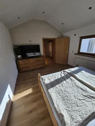Ein helles Schlafzimmer mit einem Doppelbett und einem großen Fenster. Schränke und ein Fernseher sind an der Wand platziert.
