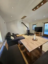 Ein gemütlicher Wohnbereich mit modernen Möbeln und einem Holztisch. Ein Fernseher und ein Kamin sorgen für eine einladende Atmosphäre.