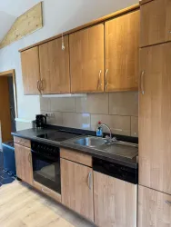 Eine moderne Küche mit Holzschränken und einem schwarzen Arbeitsplatten. Sie enthält ein Waschbecken, einen Herd und einen Kühlschrank.