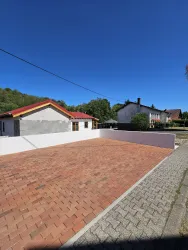 Eine klare, sonnige Aussicht auf eine gepflasterte Fläche vor einem Haus. Im Hintergrund sind mehrere Wohnhäuser und Bäume zu sehen.