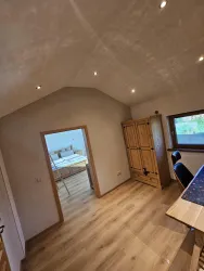 Ein heller Raum mit Holzfußboden und schräg verlaufender Decke. Auf der rechten Seite steht ein Holzschrank und ein Schreibtisch ist sichtbar.