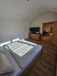 Ein helle Schlafzimmer mit einem Doppelbett und Holzboden. Ein Fernseher und ein Holzkasten sind ebenfalls sichtbar.