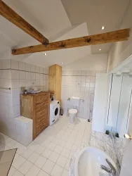 Ein modernes Badezimmer mit Holzregalen und Waschmaschine. Die Wände sind gefliest und es gibt viel Licht durch die Fenster.