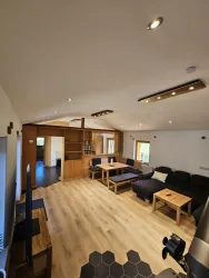 Ein modernes Wohnzimmer mit holzfarbenen Möbeln und einem großen Sofa. Der Raum ist hell erleuchtet und bietet eine offene Atmosphäre.