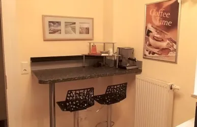 Eine moderne Kaffeetheke mit zwei schwarzen Barhockern. An der Wand hängt ein dekoratives Bild mit der Aufschrift „Coffee Time“.