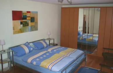 Ein gemütliches Schlafzimmer mit einem großen Bett und bunten Kissen. An der Wand hängt ein modernes Kunstwerk, und es gibt einen Spiegelkleiderschrank.