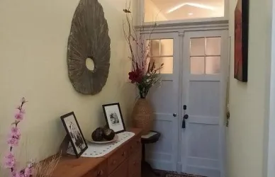 Ein einladender Flur mit Holzmöbeln und Kunstwerken an der Wand. Blumenarrangements und eine dekorative Wandinstallation verleihen dem Raum eine warme Atmosphäre.