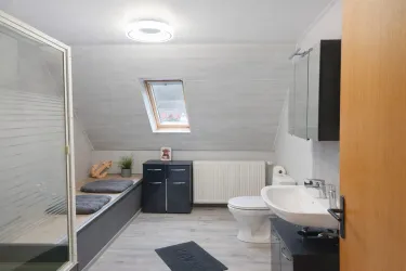 Ein modernes Badezimmer mit einer Dusche und einem Waschbecken. Es gibt einen gemütlichen Sitzbereich unter einem Dachfenster.