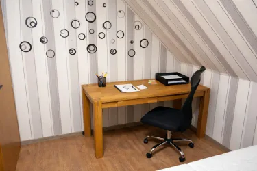 Ein gemütliches Arbeitszimmer mit einem Holzschreibtisch und einem schwarzen Bürostuhl. An der Wand sind dekorative Kreise und es gibt einige Büromaterialien auf dem Tisch.
